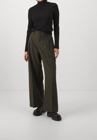 Svart ribbad långärmad topp i kombination med högmidjade, vida olivgröna byxor. Modellen bär klumpiga svarta platåskor.