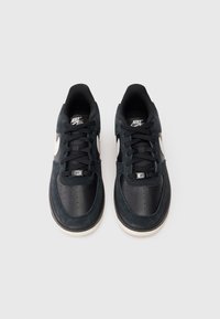 Melnas čības, kas izgatavotas no ādas un zamša, ar gludu tekstūru, apaļu purngalu, biezām auklām un baltu Nike Swoosh logo.
