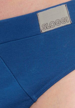 Blaue Stoffunterwäsche mit einem aufgenähten SLOGGI-Markenlabel am Bund, getragen auf heller Haut.