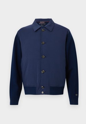 Giacca blu navy con colletto, chiusura frontale con bottoni e tessuti di diverse trame sulle maniche e sul corpo, con tasche laterali.