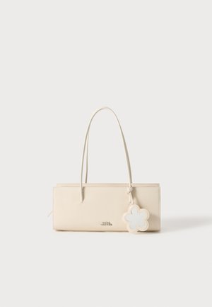 Beige lædertaske med rektangulær form, to lange håndtag og en blomstformet vedhæng. Glat tekstur og minimalistisch design.
