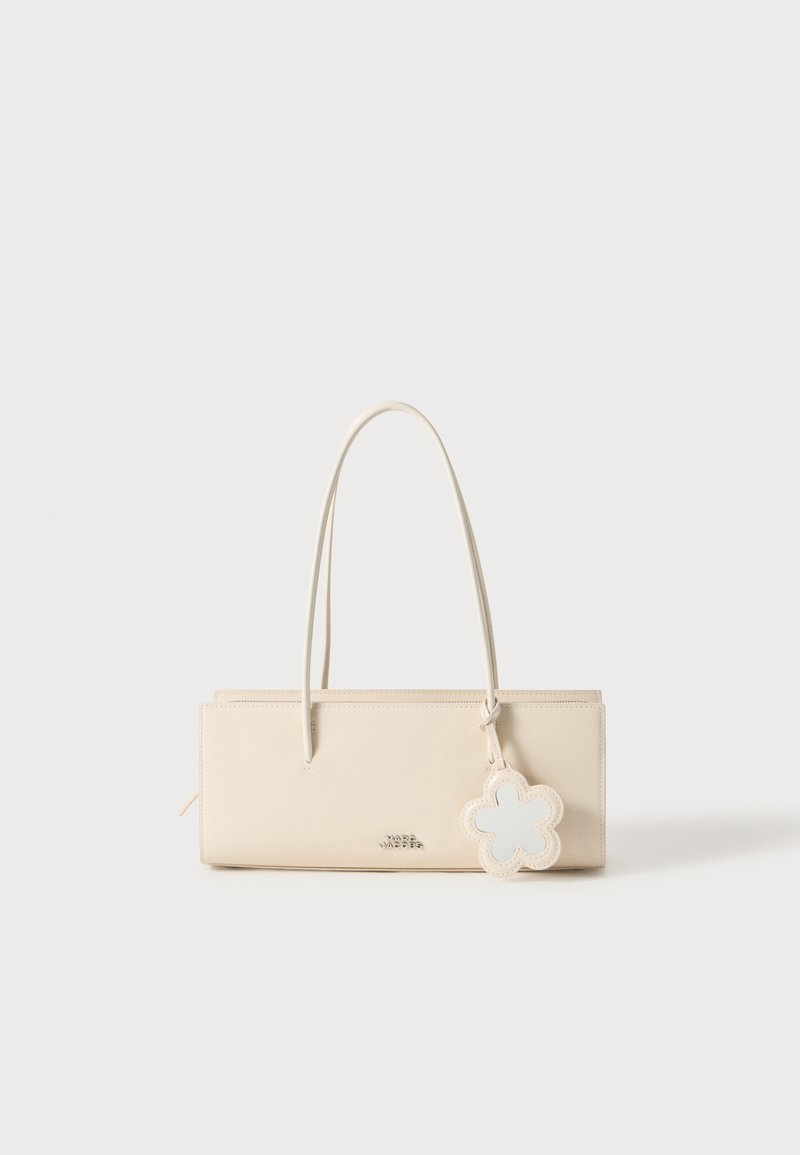 Beige nahast käekott, millel on ristkülikukujuline kuju, kaks pikka sangat ja lillekujuline ripats. Sile tekstuur ja minimalistik disain.