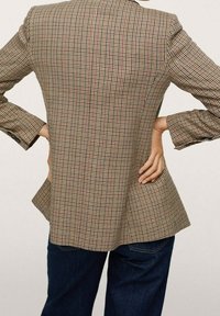 Blazer à motif écossais, doté d'une taille cintrée, de manches longues et d'un ourlet fendu. Confectionné en tissu texturé aux teintes marron, crème et rouge.