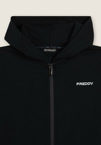 Giacca nera con cappuccio e zip, con logo Freddy sul petto e sul cursore della zip, esposta su uno sfondo chiaro e semplice.