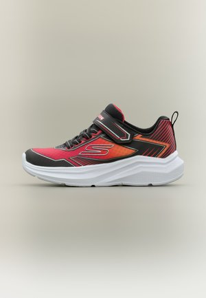 Baskets de sport rouges et noires avec semelle blanche épaisse, lacets à l'avant et bride Velcro sur fond neutre.