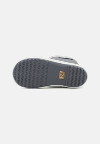 Semelle de chaussure en caoutchouc gris avec un motif texturé, contour blanc et un carré doré proéminent avec le numéro "24" gravé dessus.