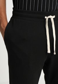 Black jogger pants made of soft fabric, featuring a ribbed waistband, side pockets, and a white drawstring for adjustment.