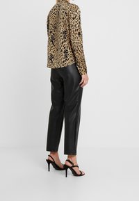 Blusa con stampa leopardata in tessuto leggero, abbinata a pantaloni in pelle nera lucida e sandali neri con tacco alto e cinturini alla caviglia.