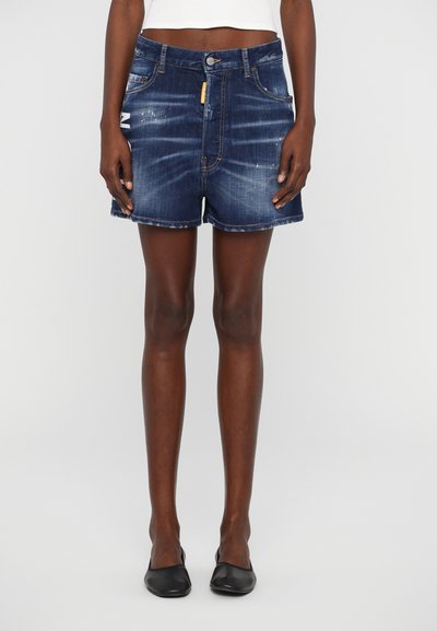 Shorts en denim avec un ourlet effiloché, conçus en bleu foncé avec des accents usés, présentant des poches avant et une étiquette jaune sur la ceinture.