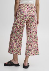 Pantalons larges à motifs floraux avec taille élastique. Présente des couleurs rose, violet et vert sur un fond jaune pâle. Tissu léger.