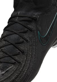 Scarpa atletica nera caratterizzata da una parte superiore testurizzata, lacci e un logo Swoosh verde a contrasto sul lato. Il design è snello e moderno.