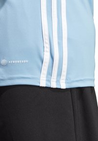 Ljusblå atletisk t-shirt med vit tre-stripsdesign på ärmen och Aeroready-logotyp. Matchas med svarta shorts.