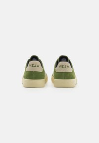 Green suede sneakers with cream accents, featuring a thick sole and the word "VEJA" embossed on the heel. Clean, minimalist design.