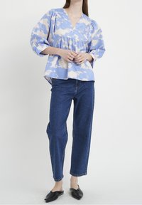 Světle modrá blůza s krémovým abstraktním vzorem, výstřihem do V a nabíranými rukávy. Spárována s tmavě modrými džíny a černými slip-on botami.