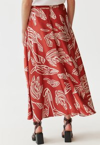 Longue jupe rouge en tissu lisse avec des motifs de feuilles abstraits blancs. Elle a une taille haute et tombe doucement jusqu'à l'ourlet.