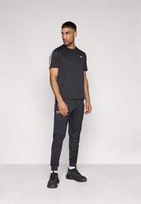 Μαύρο αθλητικό μπλουζάκι και παντελόνι jogger, με εφαρμοστή σχεδίαση. Το μπλουζάκι έχει λευκές ριγέ λεπτομέρειες στα μανίκια, σε συνδυασμό με μαύρα αθλητικά παπούτσια.