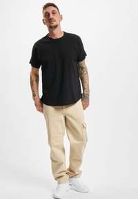 Black short-sleeve t-shirt, beige cargo pants with side pocket, and white sneakers. Casual outfit with a relaxed fit and minimal design.