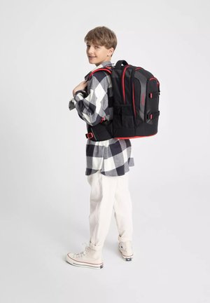 Black backpack with red accents, multiple pockets, and adjustable straps, worn by a child in a checkered shirt and cream pants.