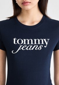 Tmavě modré bavlněné tričko s bílým nápisem "tommy jeans" v různých typech písma, krátké rukávy a kulatý výstřih.