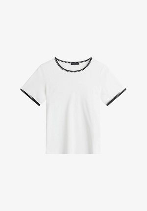 Valkoinen lyhythihainen T-paita, jossa musta siksak-reunus kaula-aukon ja hihansuun ympärillä, etuosa yksivärinen.