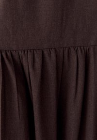 Tessuto marrone con un aspetto tessuto e strutturato. Presenta un design arricciato all'orlo, creando una silhouette morbida e fluida.
