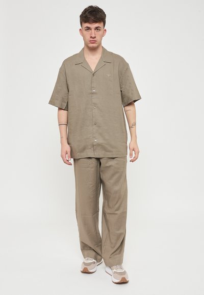 Camicia khaki a maniche corte con bottoni, dal taglio rilassato, abbinata a pantaloni larghi coordinati, realizzati in un tessuto leggero.