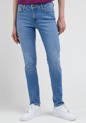 Slim-fit, jasnoniebieskie dżinsy z umiarkowanym stanem, klasyczny pięciokieszeniowy fason i subtelne efekty przetarcia. W połączeniu z białymi sneakerami.