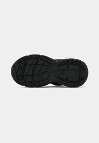 Black sneaker sole with textured tread pattern, grooves, and small circular grips for traction, shown from underneath on a white background.