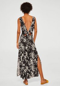 Schwarz-weißes Kleid mit einem tiefen V-Auschnitt im Rücken, in der Taille gebunden. Es hat Blattmuster, seitliche Schlitze und eine fließende Maxilänge.