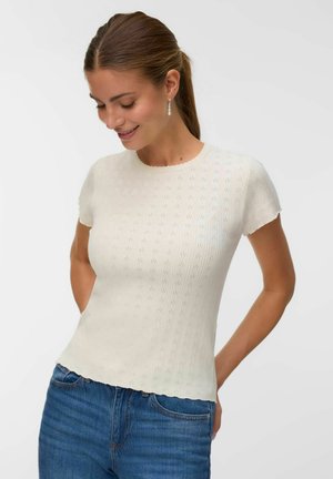 Haut créme à manches courtes en tissu tricoté texturé, présentant des rayures verticales et un col festonné. Associé à un jean bleu.