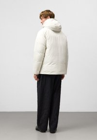 Vit vadderad jacka med huva, med en texturerad yta och en åtsittande silhuett. Matchad med lösa, mörka texturerade byxor.