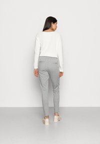 Hvit strikket genser med bred utrigning, kombinert med lysegrå joggebukser med baklommer. Modellen har på seg lysebeige platåsko.