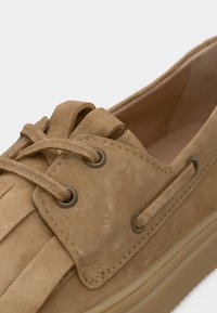 Καφέ σουέντ παπούτσι με κορδόνια, πιετά σχέδια και μεταλλικά ρυθμιστικά. Διαθέτει στρογγυλερή μύτη και επίπεδη, ταμπά ελαστική σόλα.