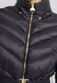 Schwarze Steppjacke mit hohem Kragen, goldfarbenem Reißverschluss und Druckknöpfen. Chevron-Steppdesign mit tailliertem Schnitt und glänzendem Finish.