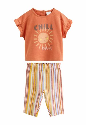 Oranžinė marškinėlių su saulės grafika ir užrašu „CHILL“, derinama su dryžuotomis geltonos, baltos ir raudonos spalvos šortais. Turi raukšlėtas rankoves ir elastingą juosmenį.