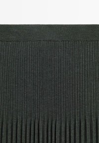 Donkergrijze geribbelde gebreide stof met een brede tailleband en verticale plooien die naar beneden lopen, wat textuur en rek creëert.