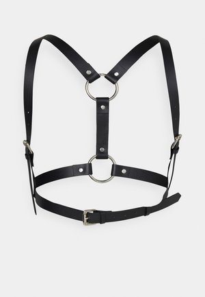 Black leather harness with adjustable straps, featuring silver metal rings and studs. The design includes a central ring and a buckle closure.