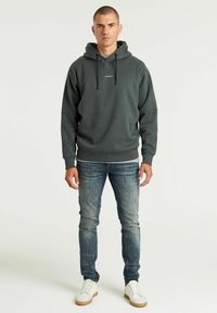 Felpa grigia scura con tasca frontale e coulisse, abbinata a jeans azzurri e sneaker bianche. Tessuto morbido, vestibilità rilassata.