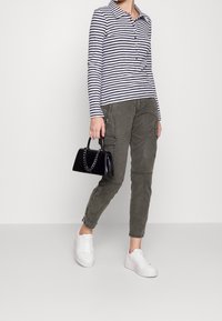 Gestreiftes Langarmshirt in Marineblau und Weiß, olivgrüne Cargo-Hose mit Reißverschlüssen, schwarze Handtasche mit Kettenhenkel, weiße Sneakers.