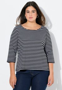 Mustavalkoraidallinen pitkähihaisuus yläosa, jossa on pyöreä pääntie ja rento istuvuus, yhdistettynä tummiin farkkuihin, mikä luo rentoa ilmettä.