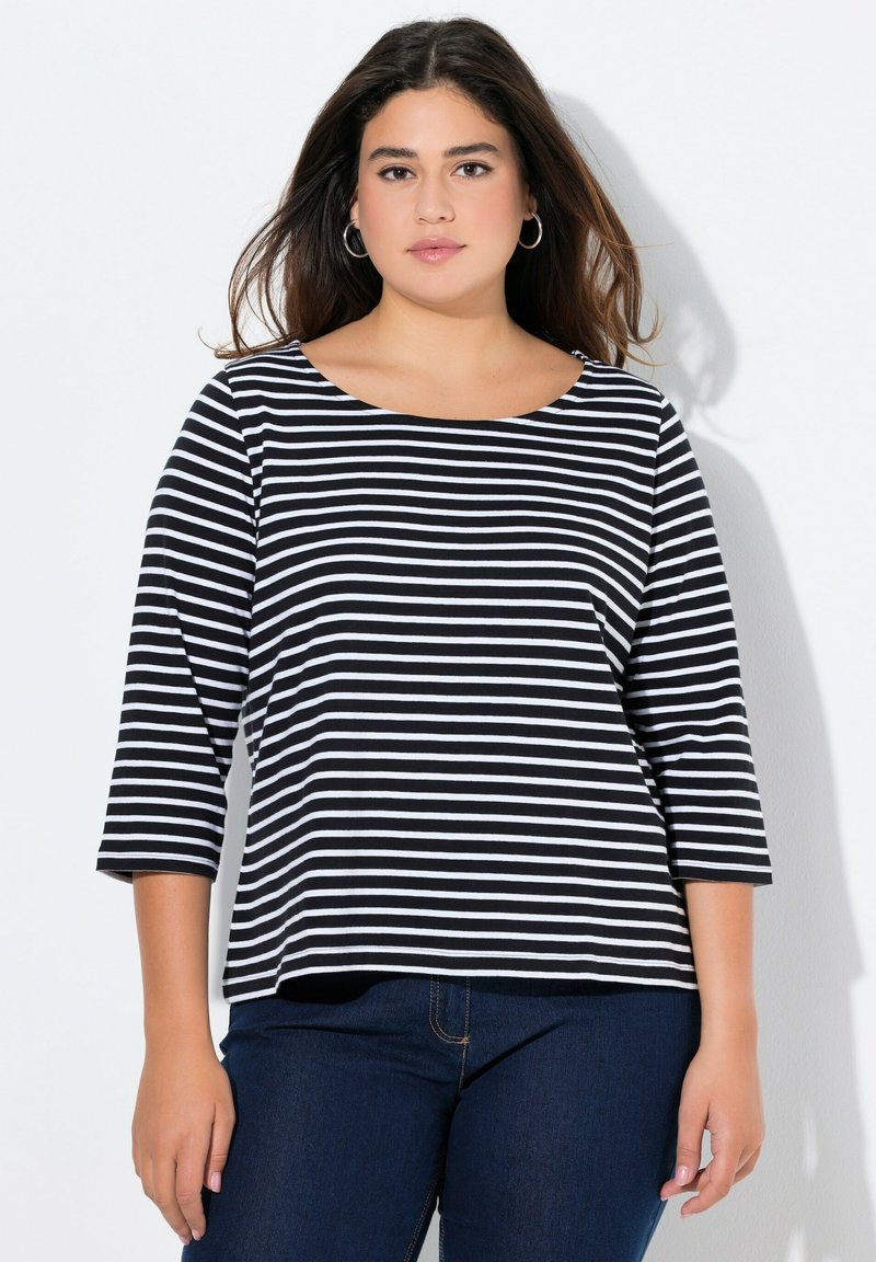 Mustavalkoraidallinen pitkähihaisuus yläosa, jossa on pyöreä pääntie ja rento istuvuus, yhdistettynä tummiin farkkuihin, mikä luo rentoa ilmettä.