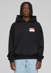 Black hooded sweatshirt with front pocket. Features a red label graphic saying “HEY! MY NAME IS” in white text. Soft fabric, relaxed fit.