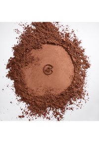 Loose and compacted cocoa powder spread in a circular shape with a small chocolate piece in the center on a white background.