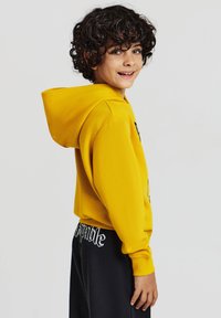 Felpa gialla con cappuccio, realizzata in tessuto testurizzato e con un design grafico. Abbinata a pantaloni della tuta neri, con lettering bianco.