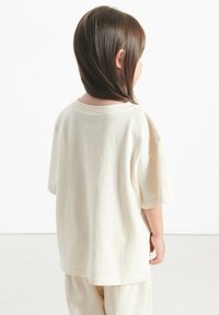 T-shirt beige clair à manches courtes avec une coupe décontractée, en coton doux, et un col rond, vu de l'arrière.