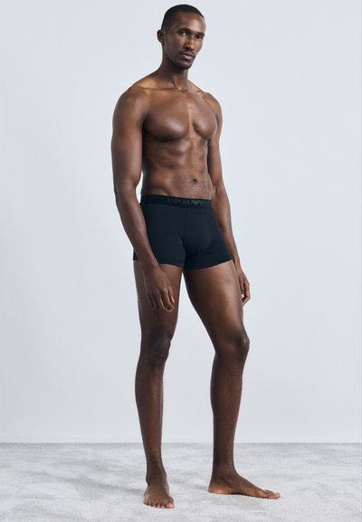 Sorte bomulds boxershorts med en blød elastik i taljen, der prydes af "Emporio Armani" logoet. Modellen har en slank fysik og er barfodet.