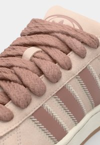 Světlounce růžová semišová teniska s tlustými, texturovanými tkaničkami, kontrastními tmavšími růžovými pruhy a bílými šicími akcenty na bocích.