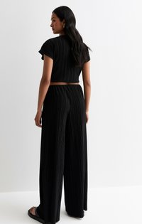 Svart kort topp och vida byxor i veckad tyg. Toppen har korta ärmar; byxorna har en elastisk midja och en flödande fall.