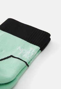 Mintgrønne sokker med sort ribbet manchet. Har hvid branding og en kontrasterende sort søm. Letvægts, struktureret strikstof.
