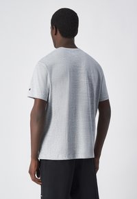 Camiseta gris de manga corta con un tejido texturizado, escote redondeado y un acento de logo en la manga. Corte casual con dobladillo recto.